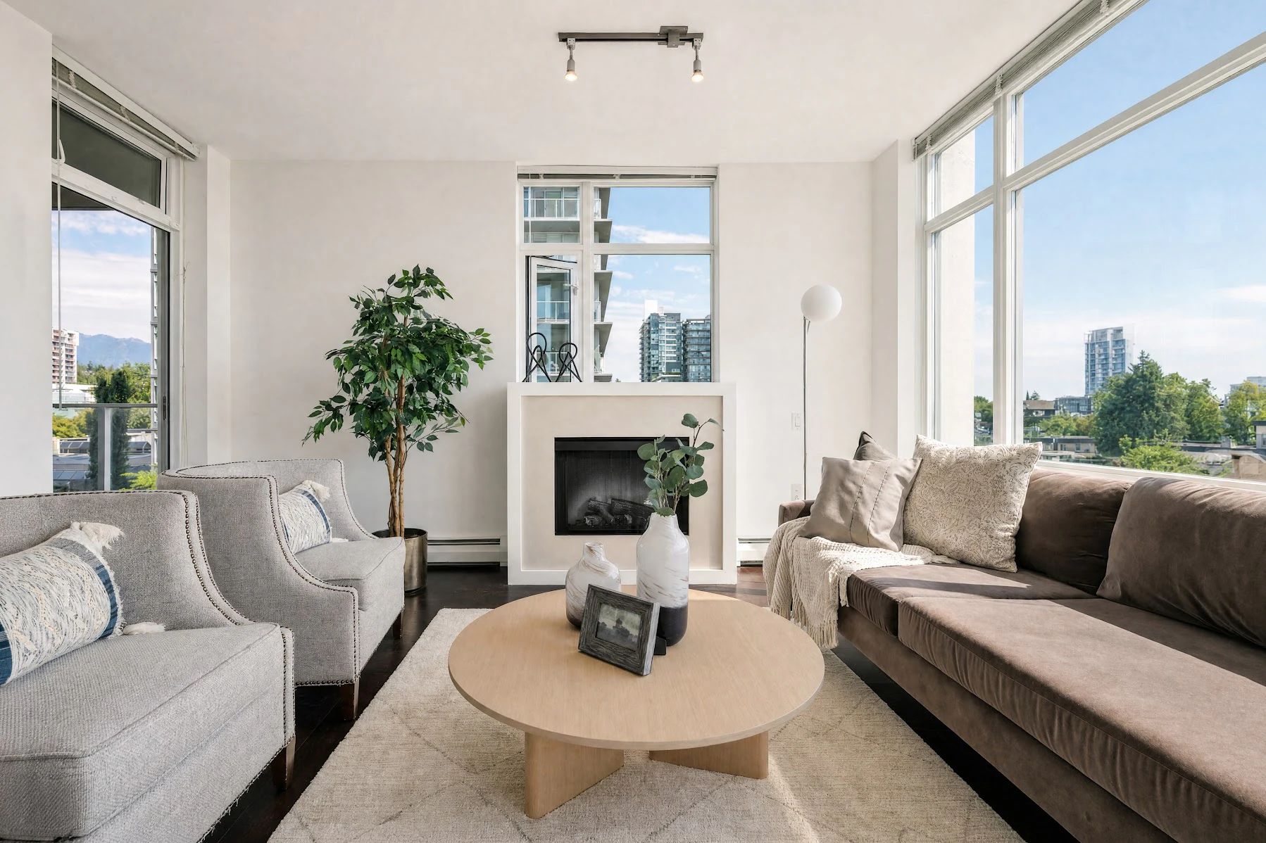 Furnished living room: armchairs and a sofa around a round coffee table, with a fireplace and city views beyond
